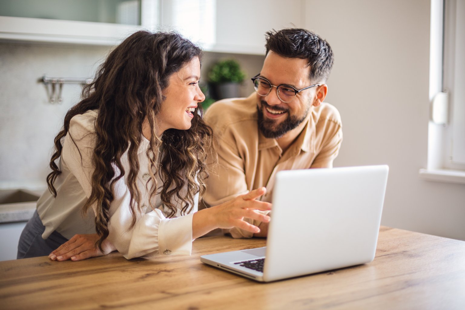 Zwei Menschen lachen und schauen bei der Arbeit auf einen Laptop in einem hellen Raum