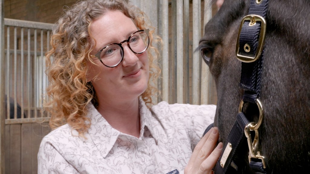 Martina Manta hält ein Pferd an einem Stall.