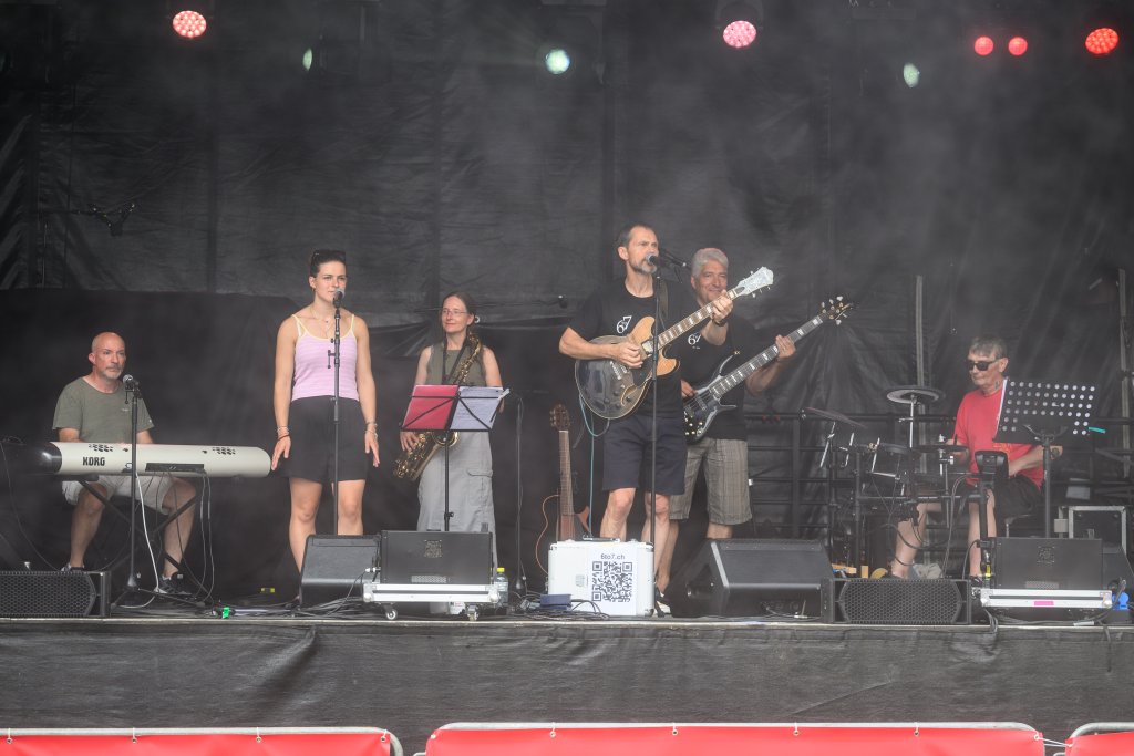 Menschen spielen auf einer Bühne mit Musikinstrumenten, im Hintergrund Licht.