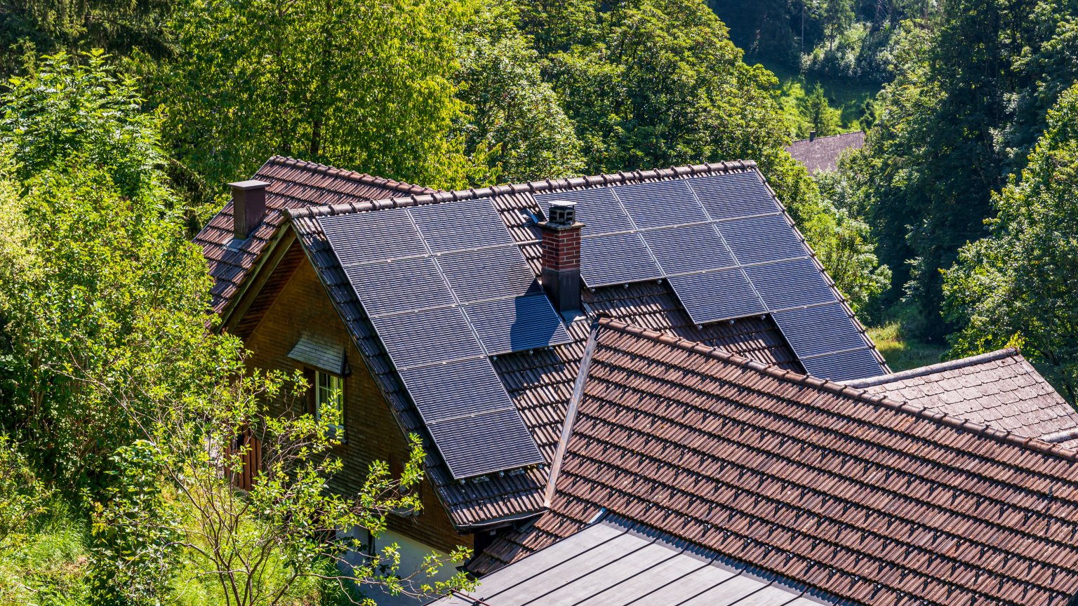 Dach mit Solarmodulen auf einem Haus in einer grünen, bewaldeten Umgebung. aus dem Artikel Energieeffizient bauen und renovieren: So sparen Sie Kosten und Energie