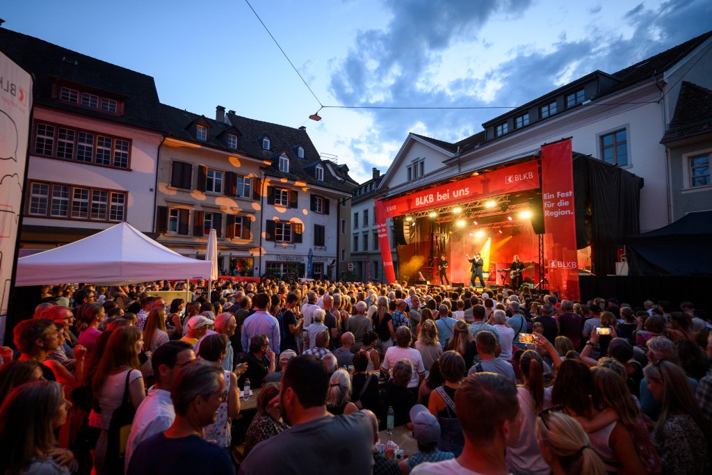 In der Stadt versammeln sich Menschen bei einem Open-Air-Konzert auf einer Bühne bei Sonnenuntergang.