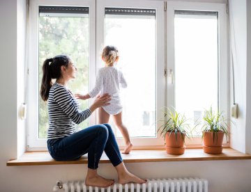 Eine Mutter beobachtet mit ihrem Kind die Aussicht durch ein Fenster. aus dem Artikel Energieeffizienz beim Bauen und Renovieren – es lohnt sich