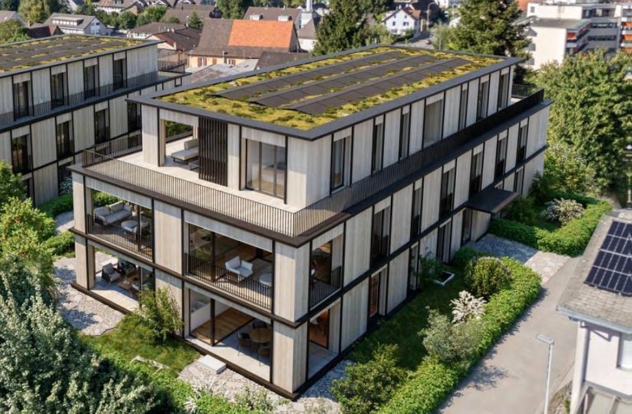 Mehrstöckiges Gebäude mit großen Fenstern, Balkonbereichen und begrünten Flächen auf dem Dach