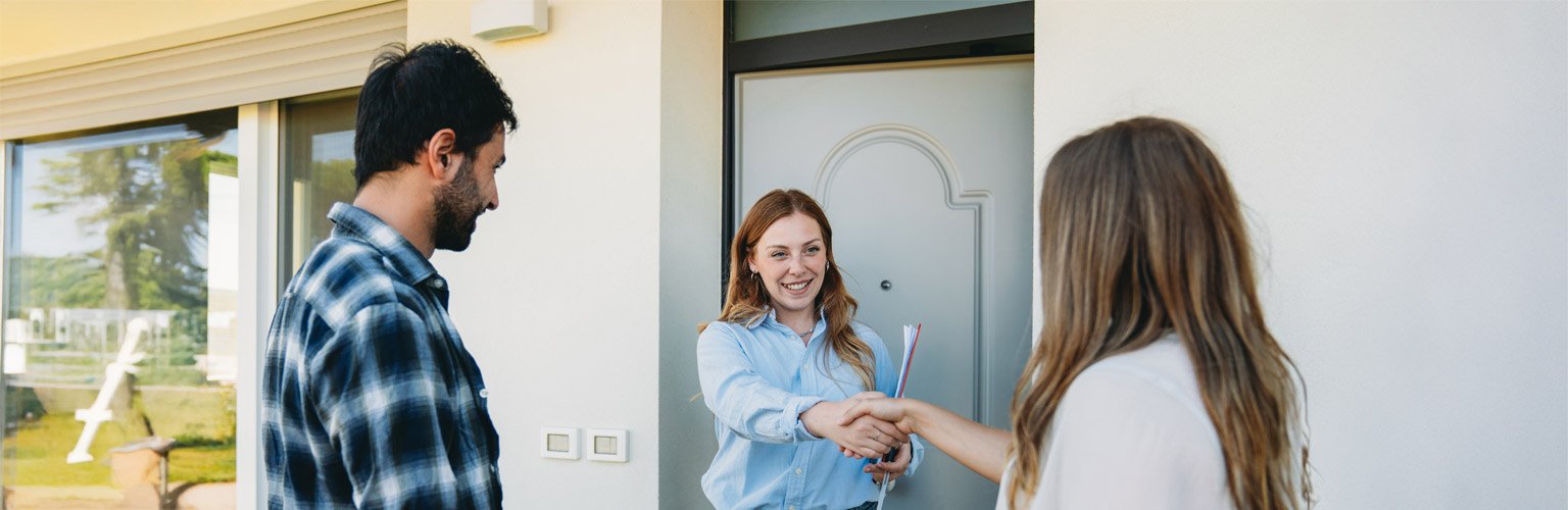 Händedruck einer Immobilienmaklerin vor der Grundstückseinfahrt. Menschen stehen vor dem Haus