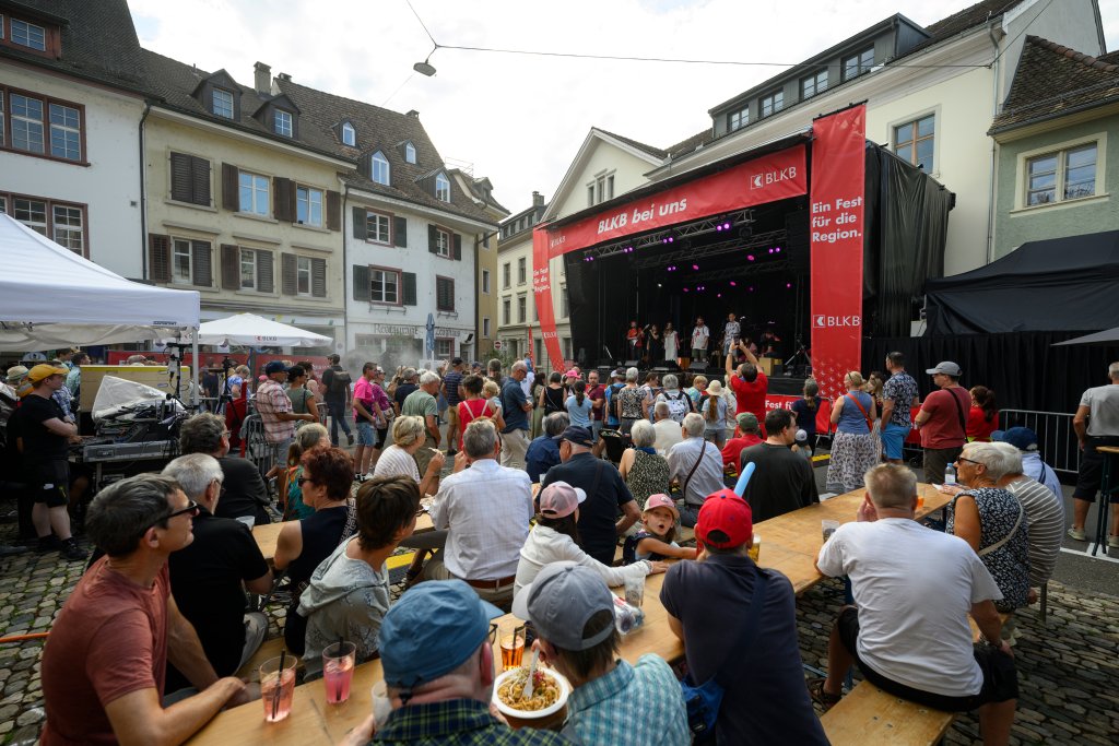 Viele Menschen stehen vor einer Bühne bei einem Open-Air-Konzert auf Kopfsteinpflaster.