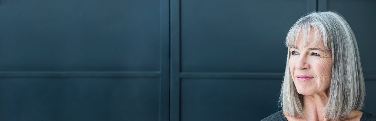 Eine nachdenkliche Frau mit grauen Haaren vor einem eleganten Hintergrund.