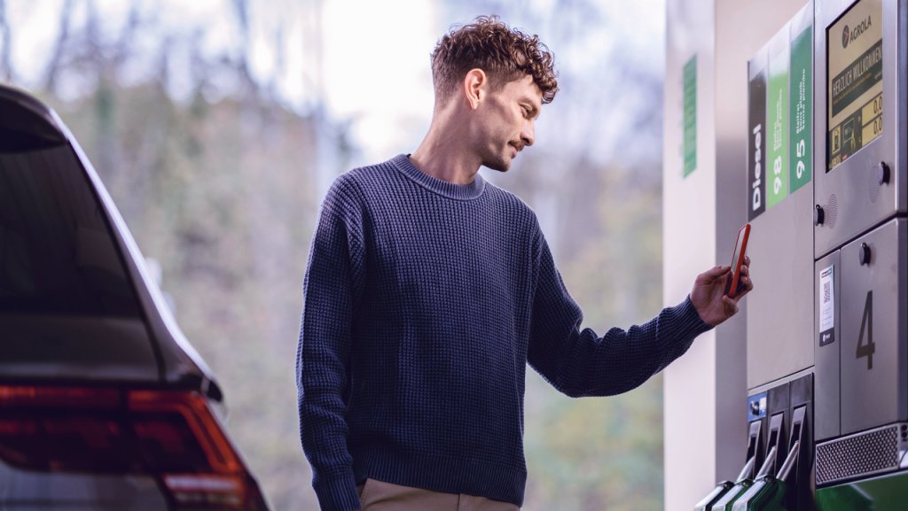 Ein Mann nutzt sein Smartphone an einer Tankstelle.