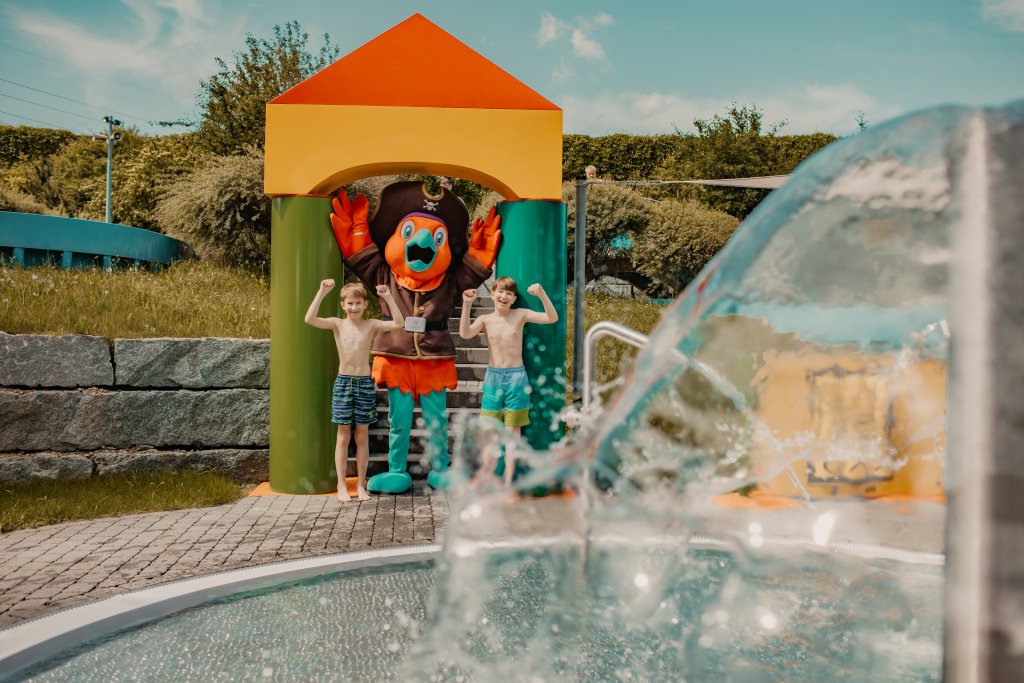 Zwei Kinder mit Clown-Charakter an Wasserspiel, im Freien, sonniger Tag, spielend.