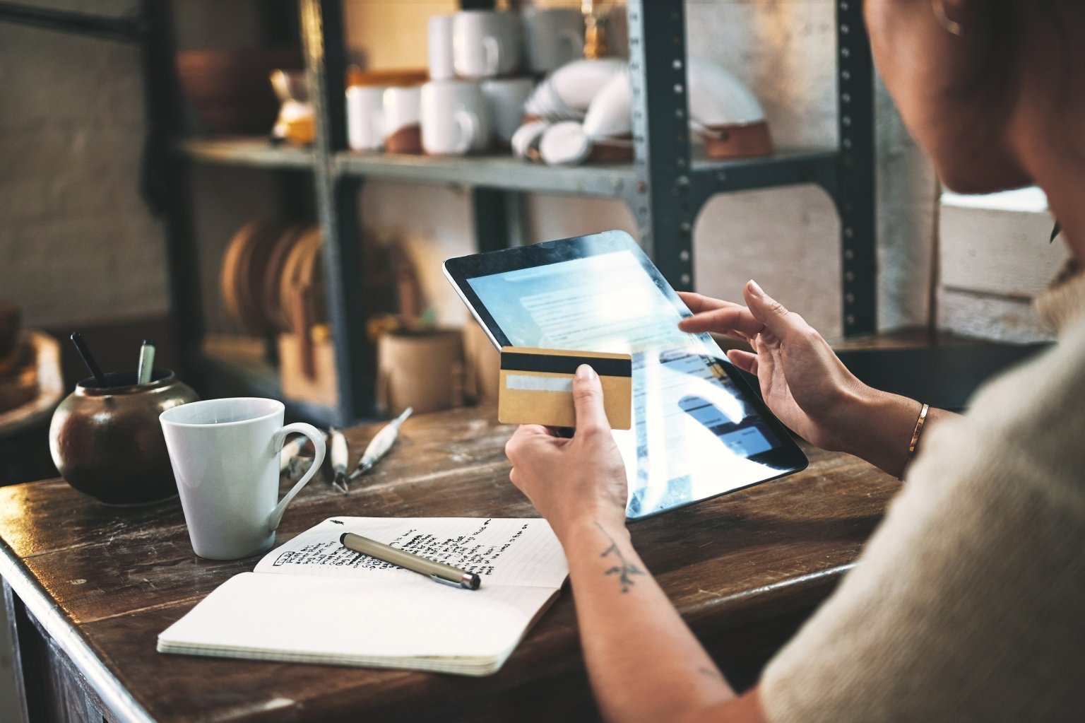 Eine Person nutzt ein Tablet an einem Arbeitstisch mit Notizbuch, Tasse und Küchenutensilien. aus dem Artikel Welche Karte gibt mir maximale Sicherheit und Flexibilität?