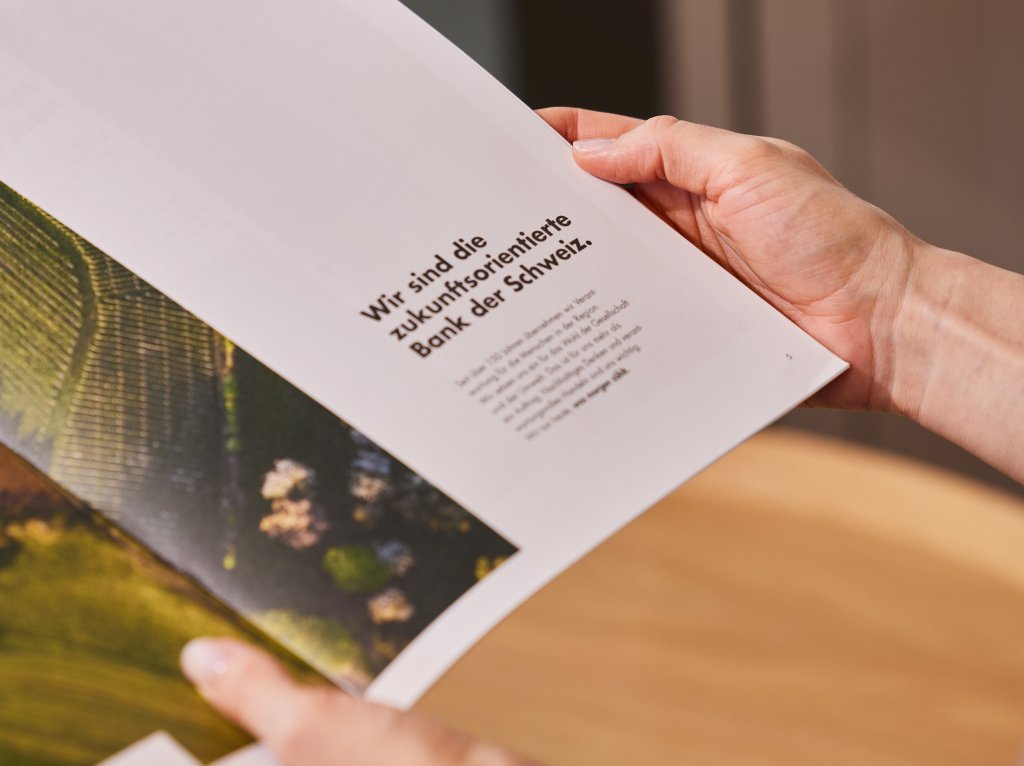 Eine Person liest eine Broschüre des Nachhaltigkeitsbericht. Im Titel steht 'Wir sind die zukunftsorientierte Bank der Schweiz'.