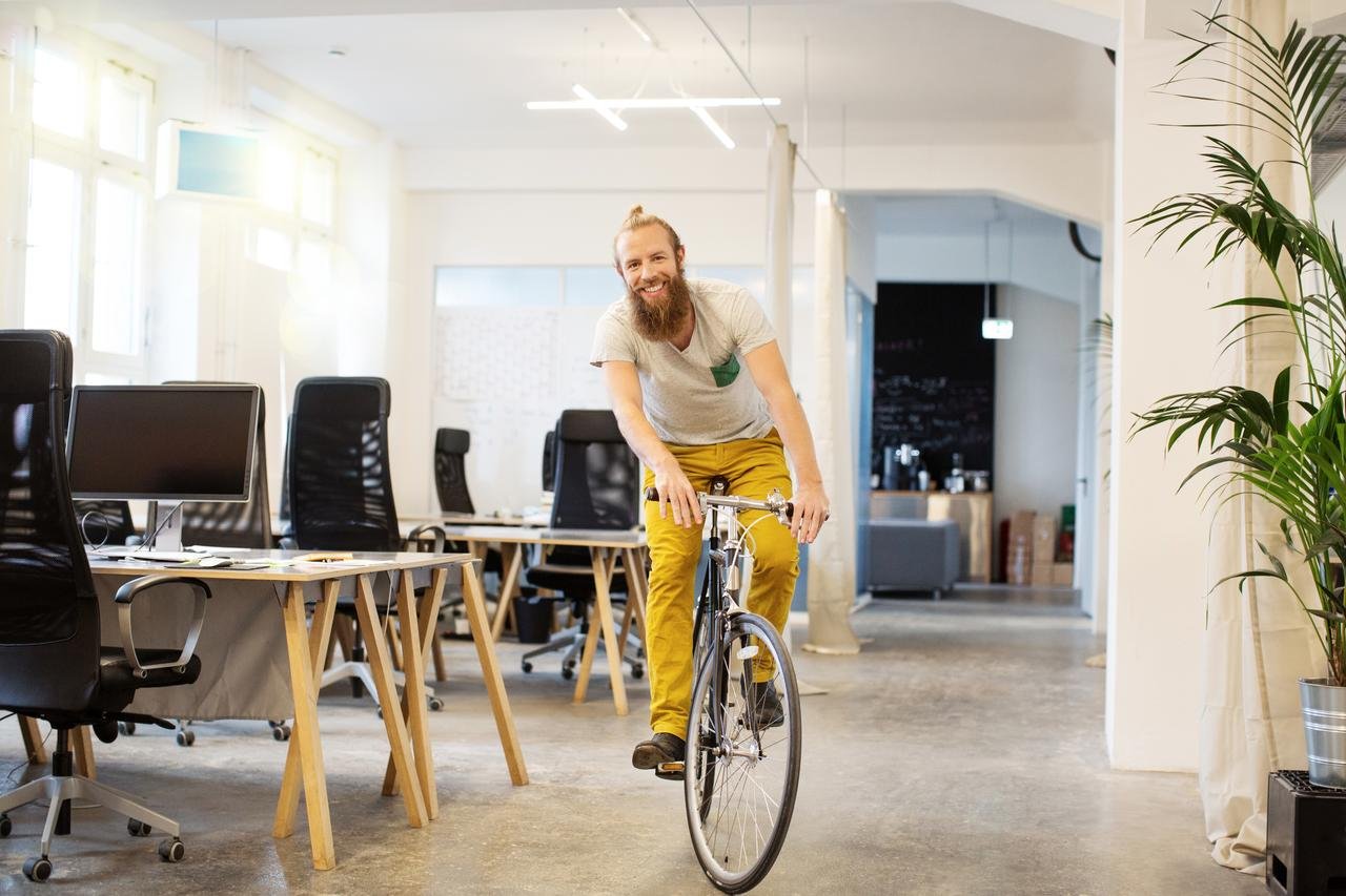 Glücklicher junger Mann fährt mit seinem Fahrrad durch ein Startup Büro