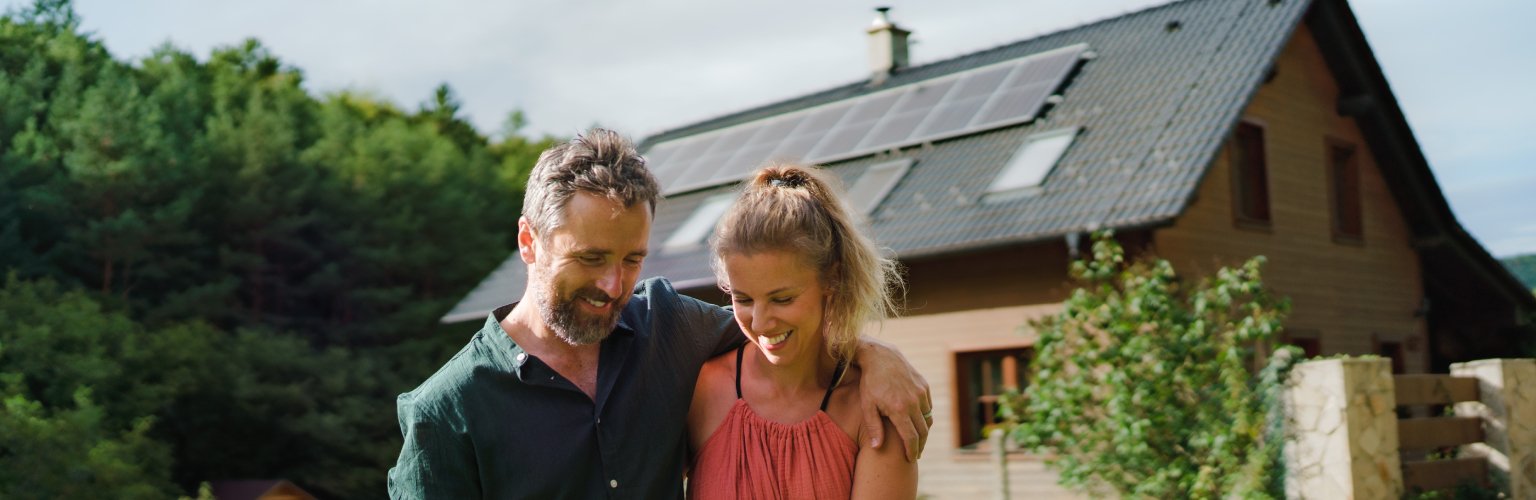 Ein Mann und eine Frau stehen vor einem Haus in einer grünen Natur.