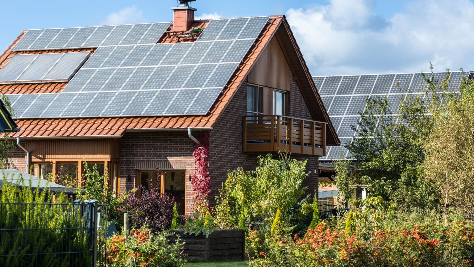 Modernes Wohnhaus mit Solaranlage, umgeben von blühenden Pflanzen in ruhiger Nachbarschaft.