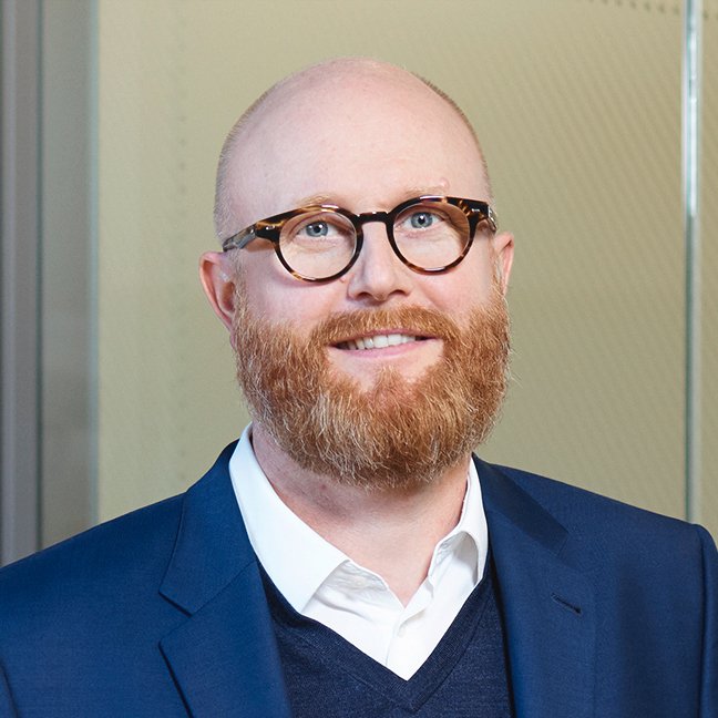 Mann in dunklem Anzug mit weißem Hemd, professionelles Umfeld, BLKB Logo im Hintergrund