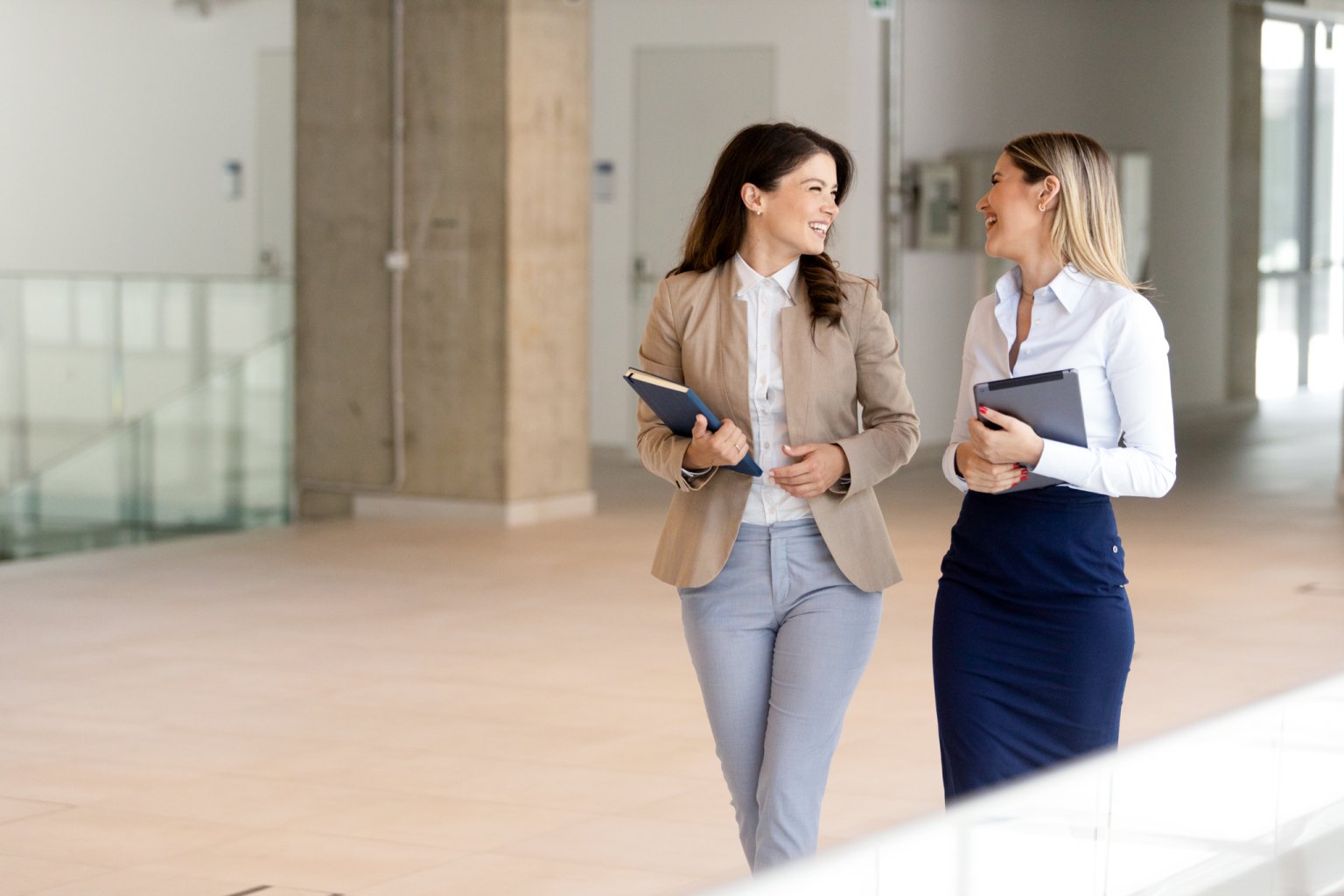 Zwei Unternehmerinnen gehen und unterhalten sich in einem modernen Büroraum.