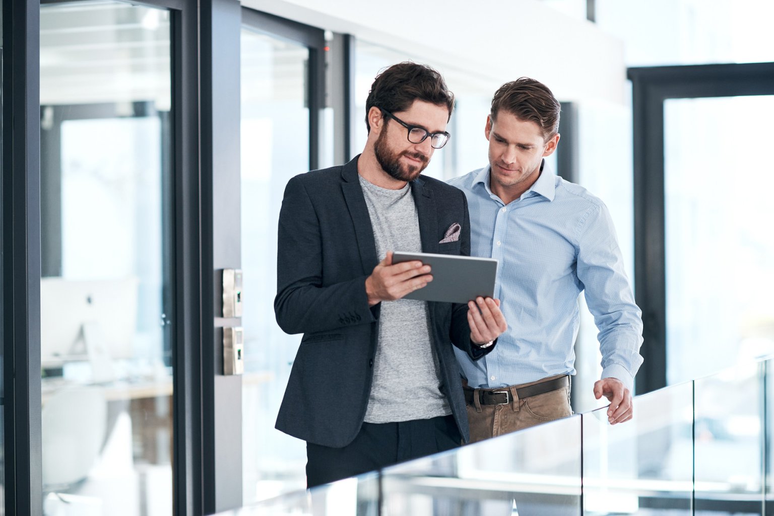 Zwei Männer besprechen in einem modernen Büro eine Planung auf dem Tablet.