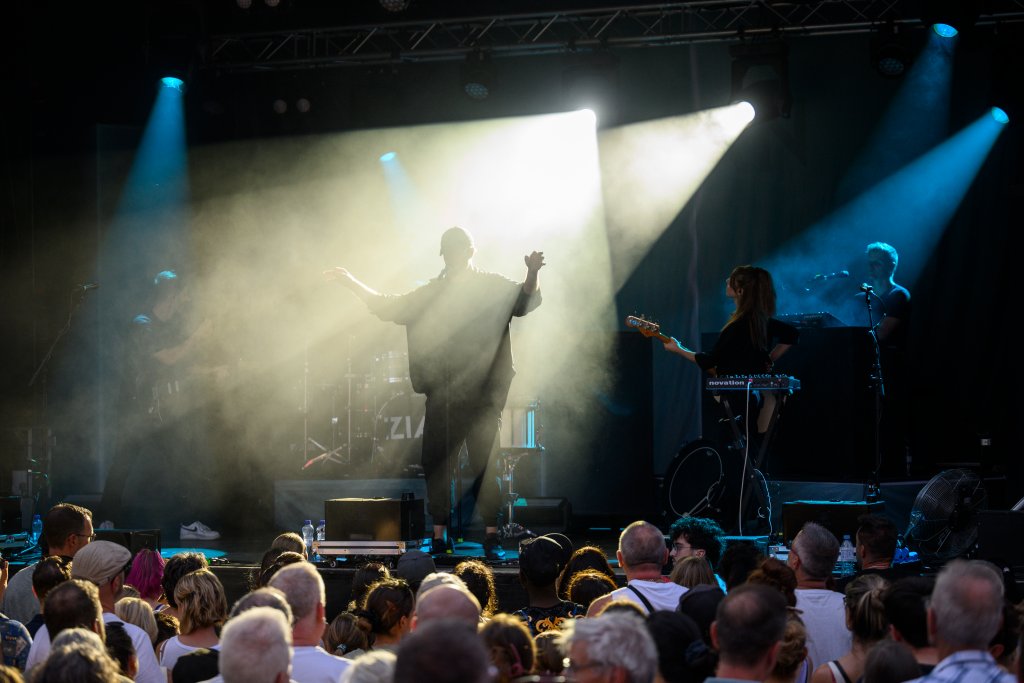 Auf der Bühne performen Musiker bei Bühnenlicht, das Publikum schaut zu.