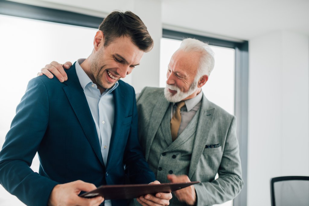 Zwei Männer lachen und schauen auf ein Tablet in einem hellen Büro.