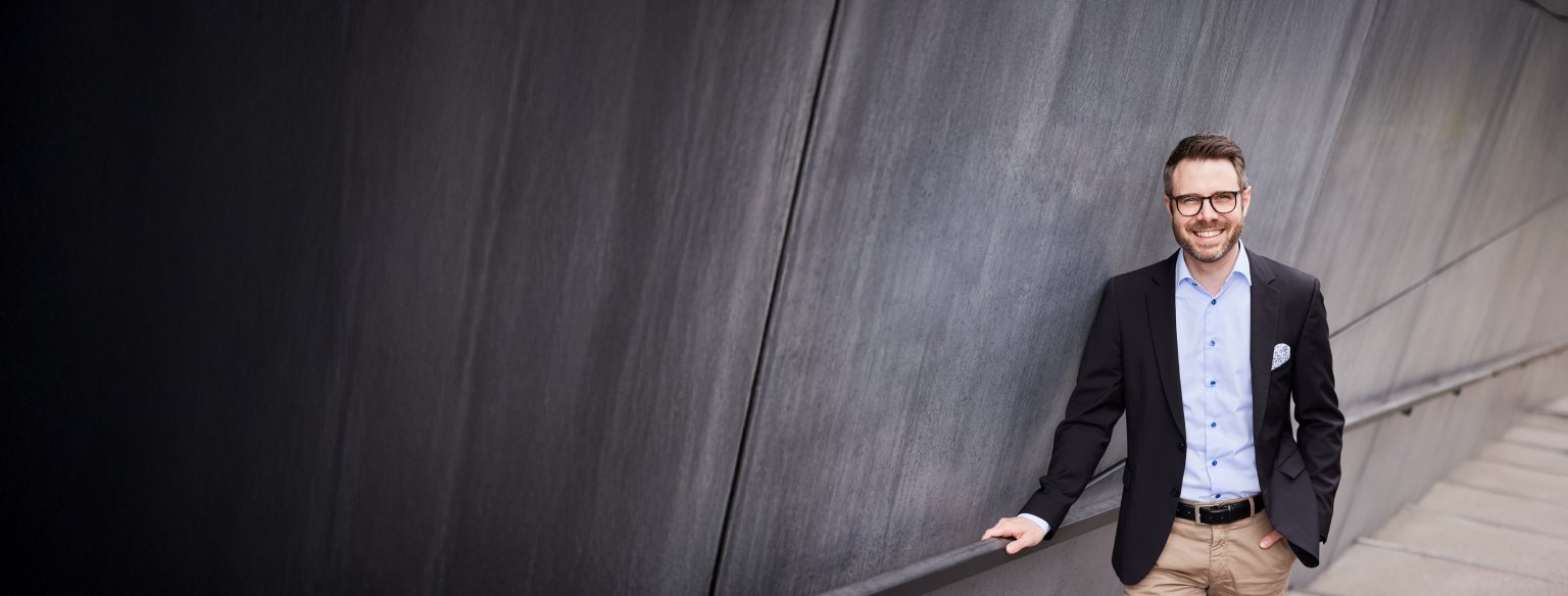 Ein Mann im Anzug lächelt an einer modernen Wand der Basellandschaftlichen Kantonalbank (BLKB).