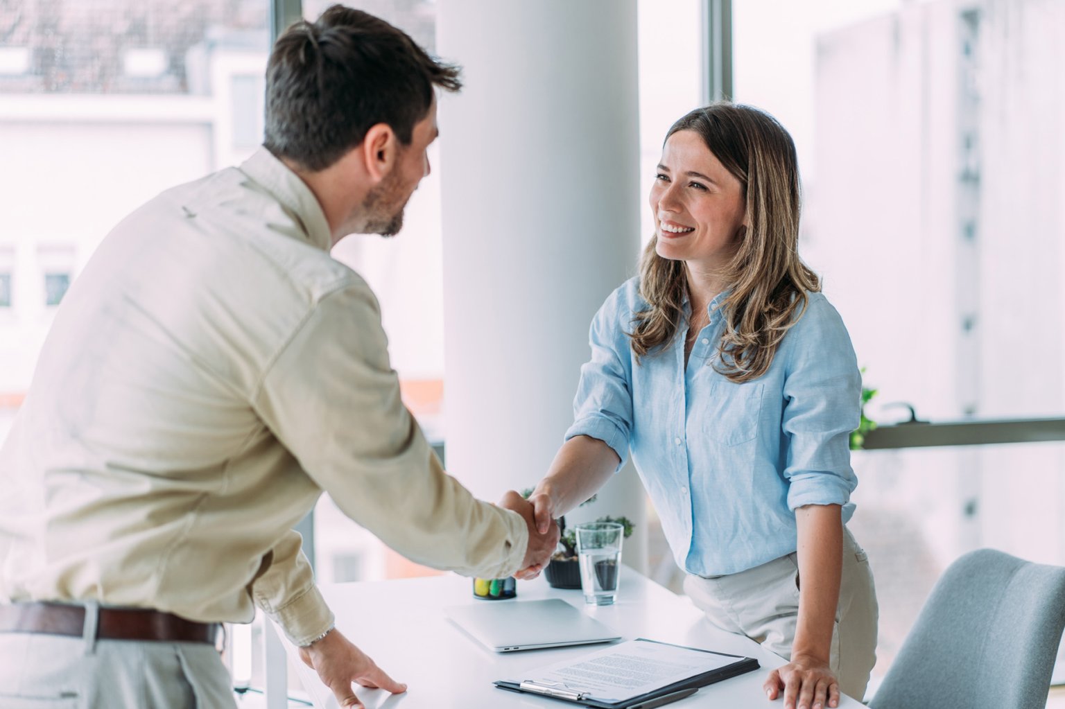 Zwei Personen in einem modernen Büro bei einem freundlichen Gespräch und Händedrücken.