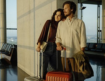 Ein Paar wartet am Flughafen mit Gepäck auf den Flug zu ihrem nächsten Abenteuer. aus dem Artikel Beim Einkaufen oder Reisen: So profitieren Sie mit Ihrer Kreditkarte