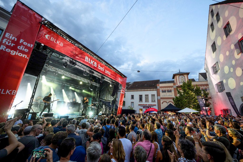 Ein großes Konzert mit Bühne, Licht, Menschenmenge im Freien, umgeben von Gebäuden aus dem Artikel