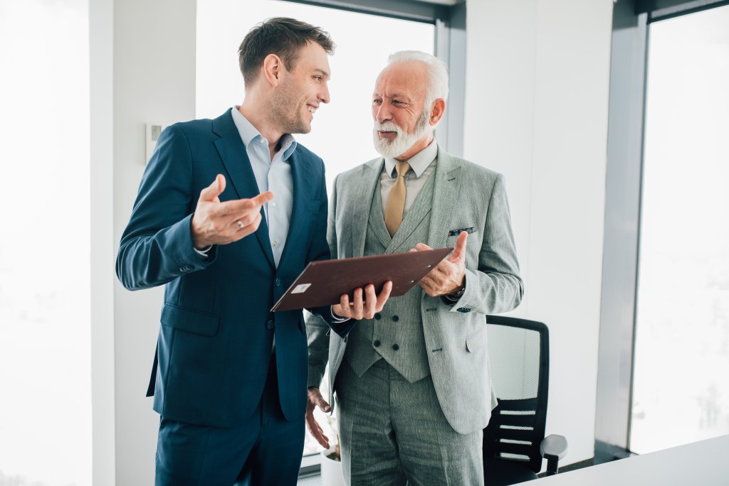 Zwei Geschäftsleute, die sich in einer Gespräch befinden, einer hält ein Portfolio in einem Büroumfeld.
