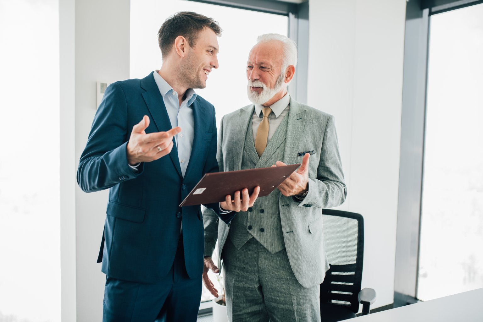 Zwei Geschäftsleute, die sich in einer Gespräch befinden, einer hält ein Portfolio in einem Büroumfeld.