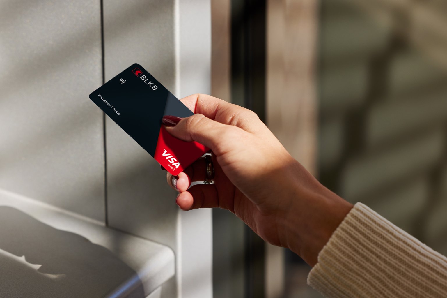 Eine junge Frau möchte mit ihrer BLKB-Karte Geld an einem Automaten abheben.