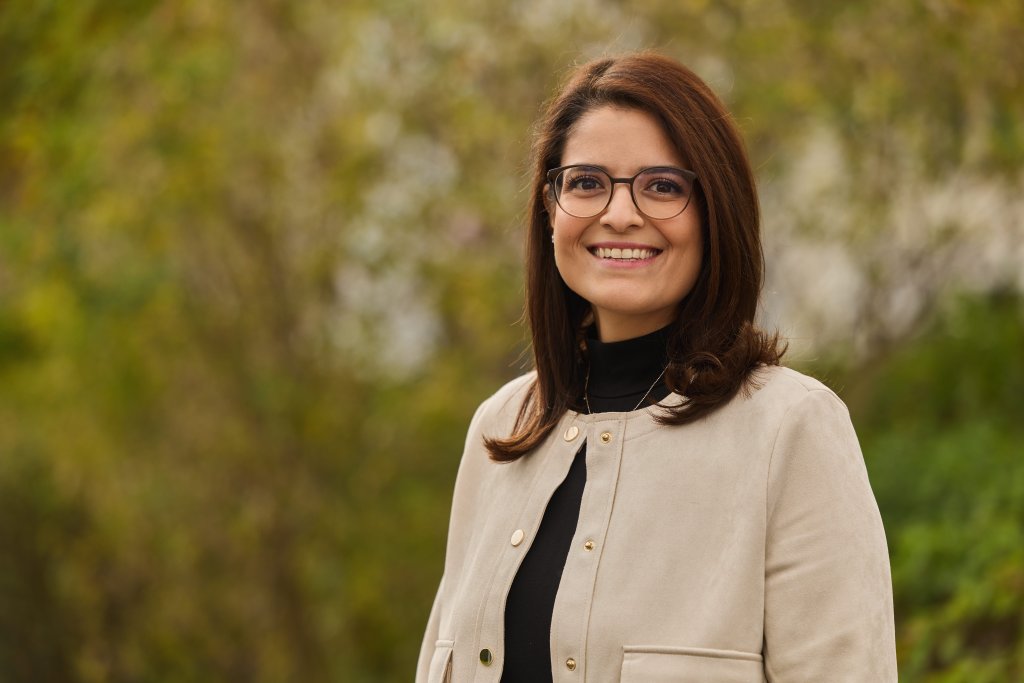 Betül Karabulut steht im Freien, trägt beige Jacke vor grünem Hintergrund.