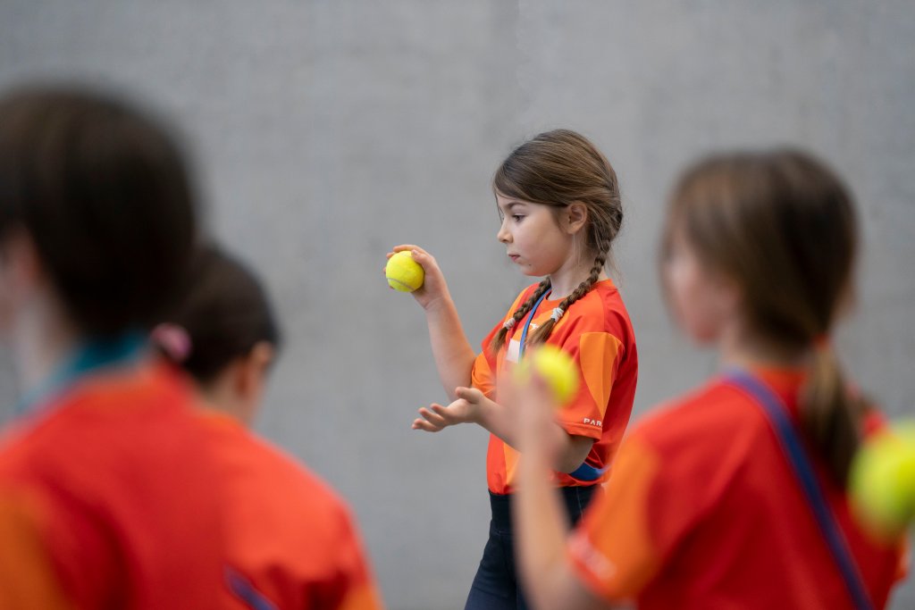 Kinder beim Tennis, lachend und in roten Sportshirts, auf einem Court.