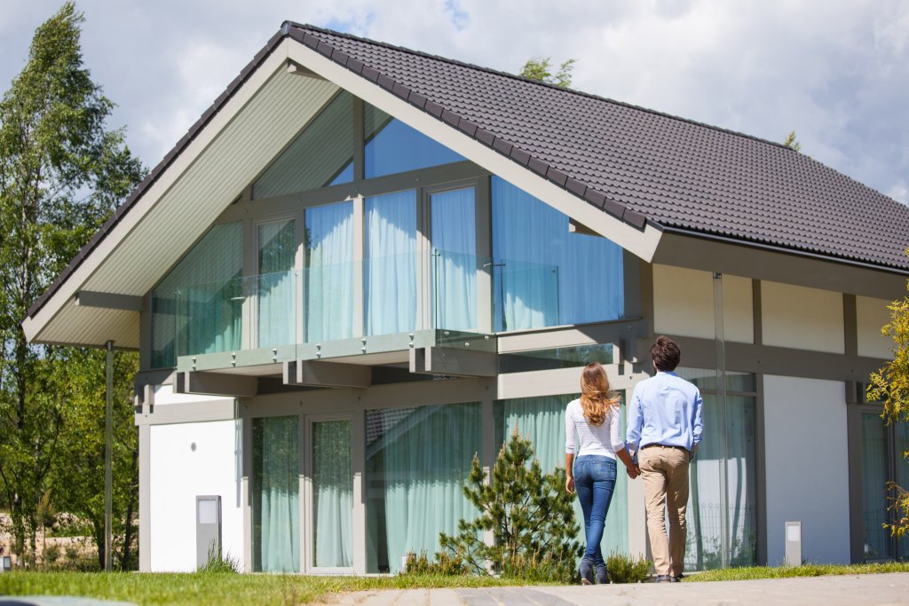 Ein Paar geht auf ein modernes Haus mit grossen Fenstern und einem schrägen Dach zu.