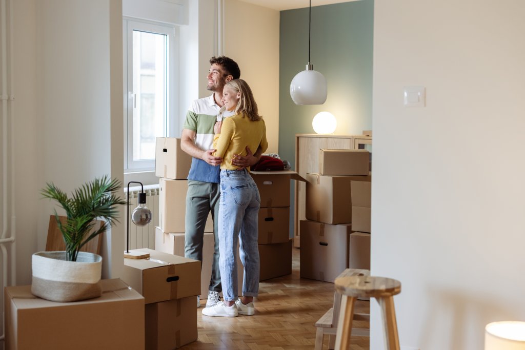 Zwei Menschen stehen in einer helle, moderne Wohnung, umgeben von Umzugskartons.