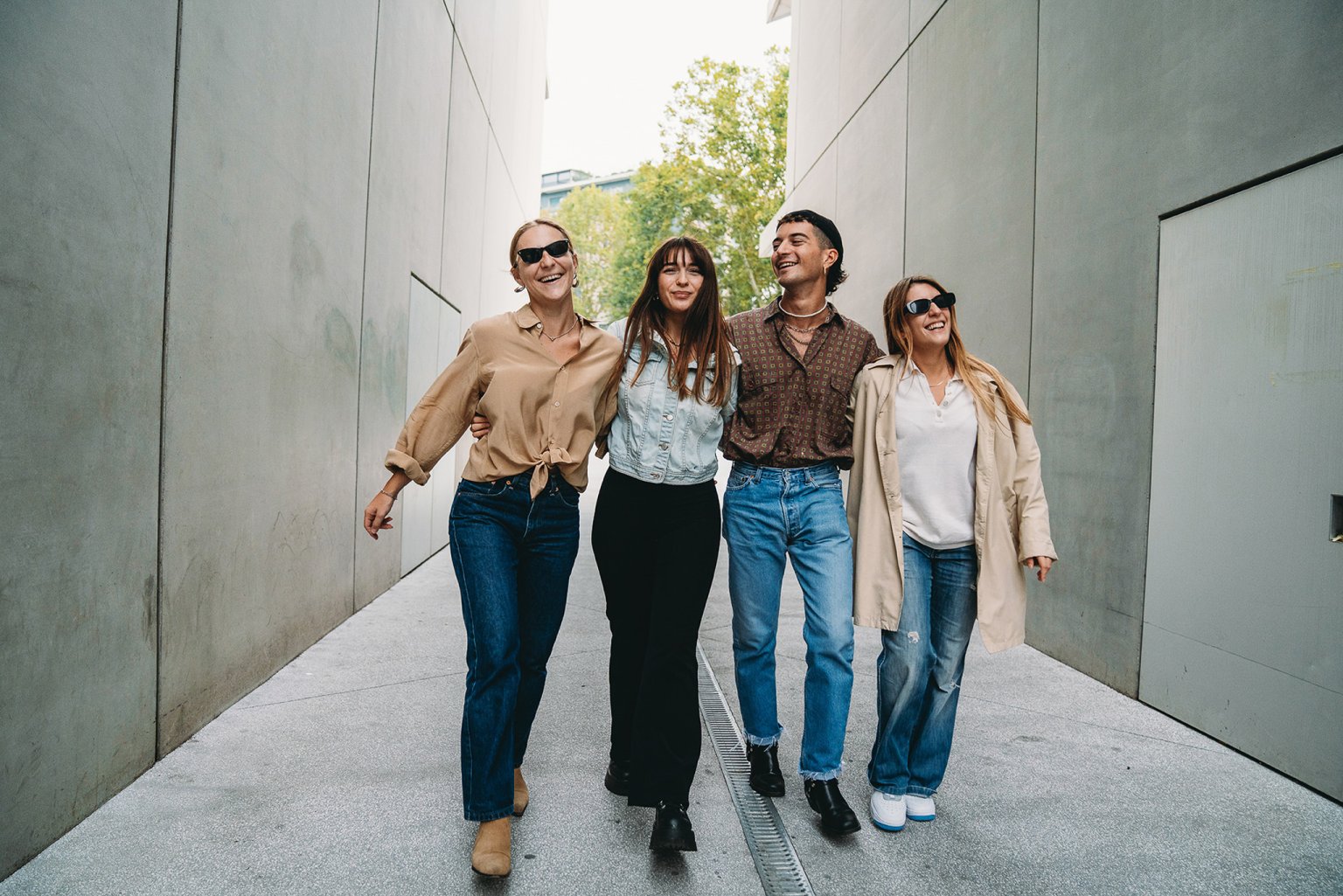 Vier junge Menschen gehen fröhlich durch eine moderne Stadtlandschaft.