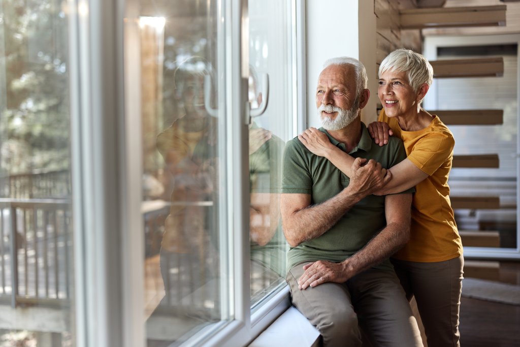 Zwei Personen sitzen am Fenster, im Hintergrund ist die Inneneinrichtung zu sehen.
