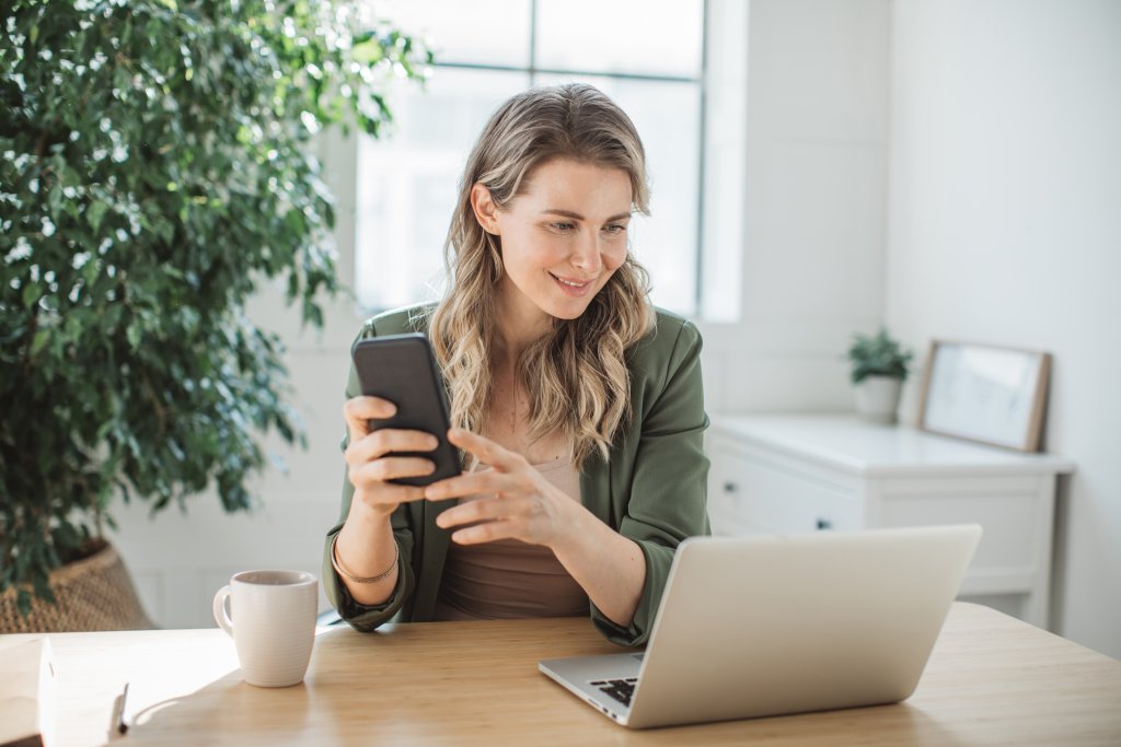 Frau mit Handy und Laptop im Büro bei der Basellandschaftlichen Kantonalbank