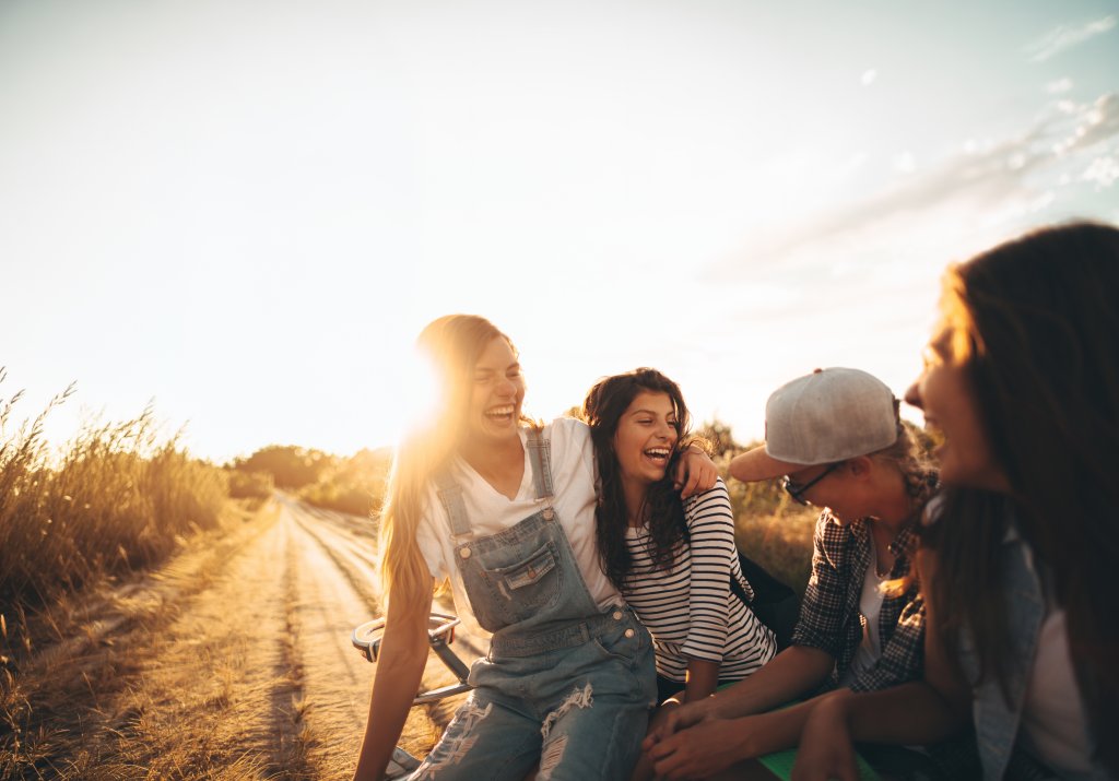Vier Menschen lachen und sitzen auf einer Wiese, im Sonnenlicht bei Sonnenuntergang. aus dem Artikel
