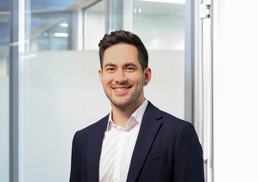 Ein Mann trägt Anzug und steht vor einer Glaswand im Büro.