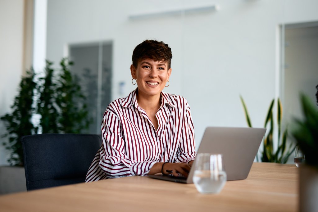 Frau arbeitet an Laptop im modernen Büro, hinter ihr Pflanzen und helle Wände.