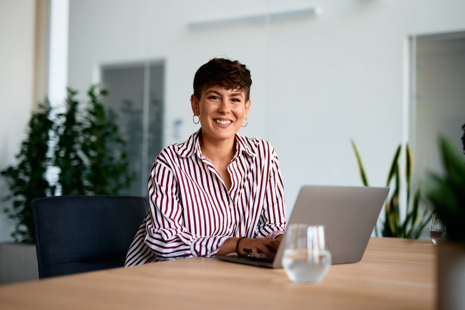 Frau arbeitet an Laptop im modernen Büro, hinter ihr Pflanzen und helle Wände.