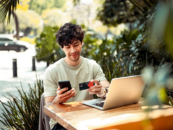 Ein junger Mann bezahlt in einem Restaurant auf der Terrasse seine Rechnungen mit einer BLKB Karte.