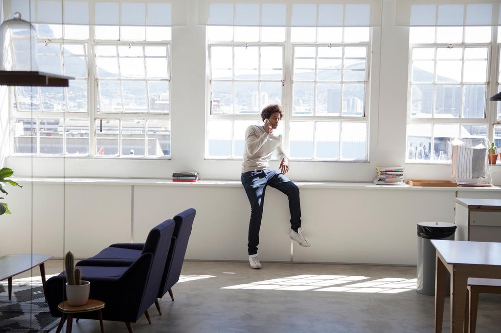 Moderner Arbeitsplatz mit hellen Möbeln und entspannter Atmosphäre. Ein Mann telefoniert mit einem Kunden.