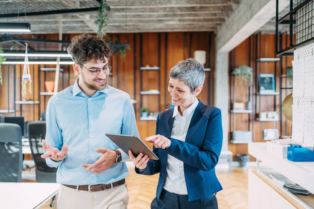 Aufnahme von zwei überzeugten Geschäftsleuten, die am Arbeitsplatz sprechen. Zwei Kollegen, die beim Gehen in einem modernen Büro ein digitales Tablet verwenden. Geschäftsmann und Geschäftsfrau in der Sitzung, die Geschäftsstrategie besprechen.