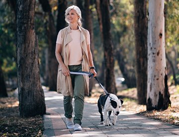 Eine Frau geht mit ihrem Hund auf einem Weg in der Natur. aus dem Artikel Wie sorge ich heute für morgen vor?