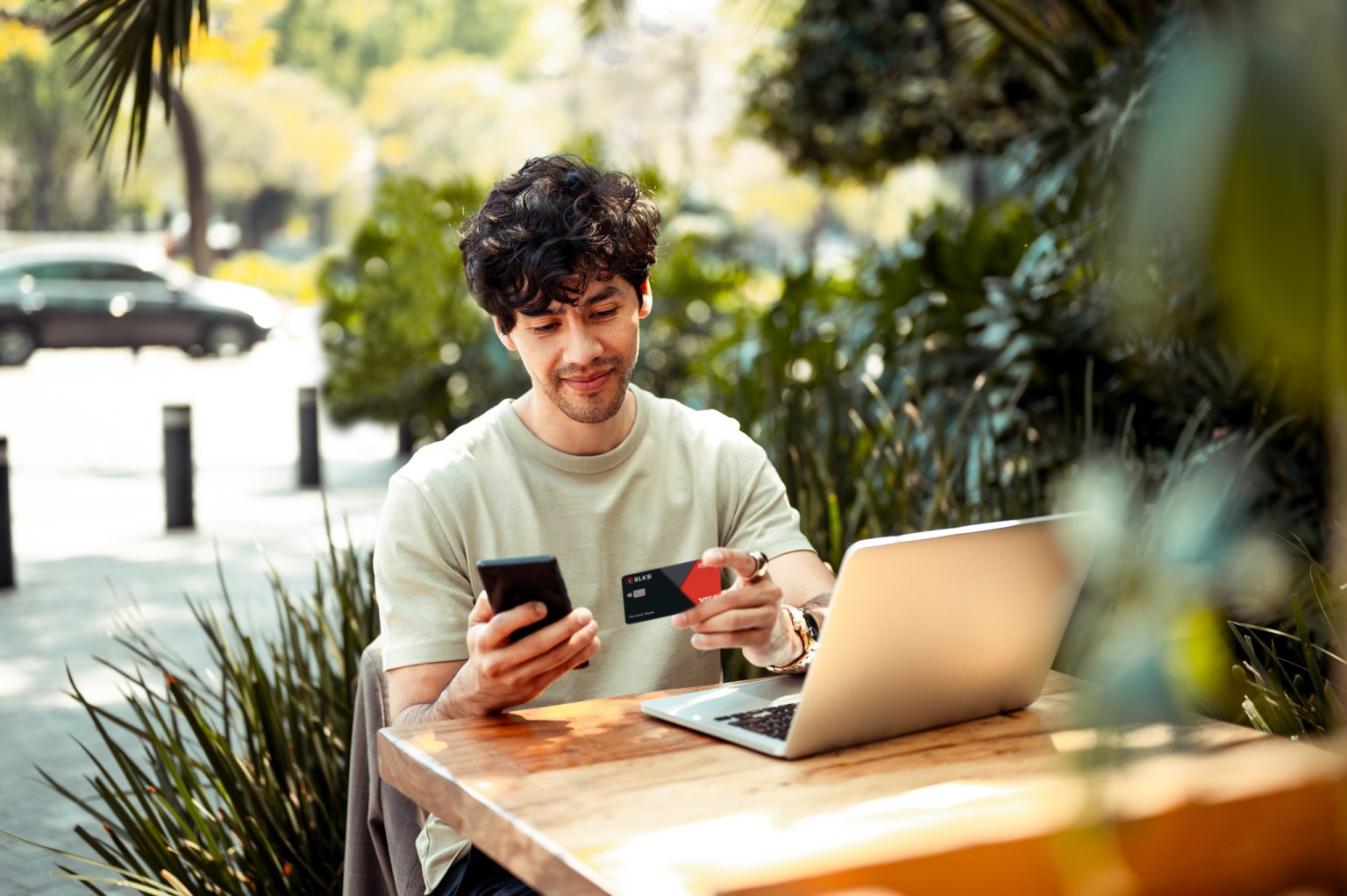 Ein junger Mann bezahlt eine Online-Rechnung mit seiner BLKB-Karte. Er sitzt in einem Café.