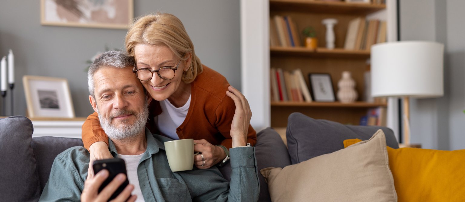 Ein Mann und eine Frau sitzen auf einem Sofa, schauen auf ein Smartphone.