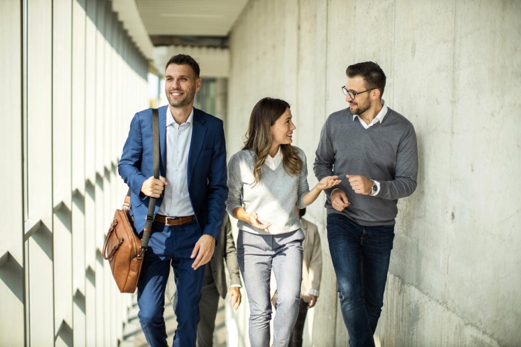 Eine Gruppe von drei glücklichen Geschäftsleuten unterhält sich, während sie durch die Lobby eines modernen Bürogebäudes gehen.