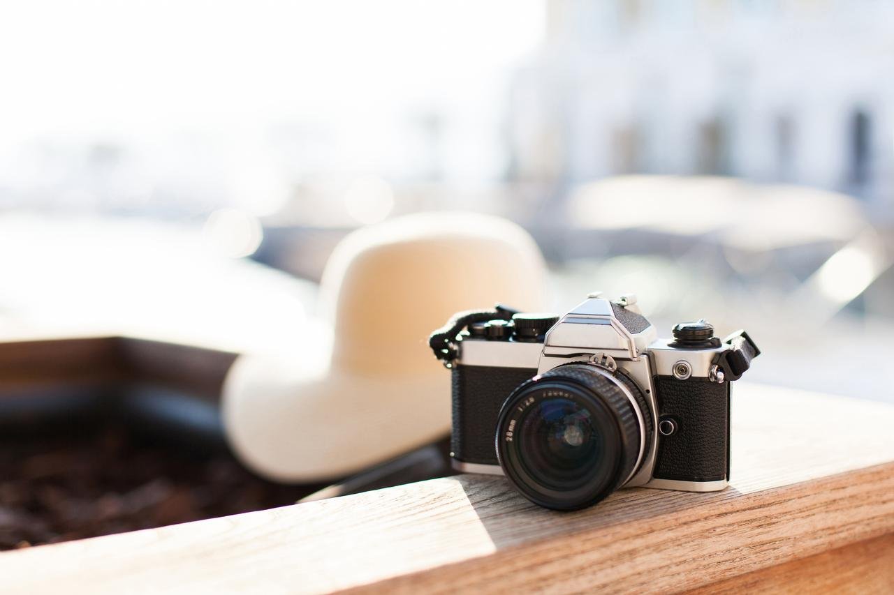Retro-Filmfotokamera und Strohhut liegen bei Sonnenuntergang im Badeort im Freien. Urlaubs-, Touristen- und Reisekonzept. Unscharfer heller Hintergrund mit Platz für Text. aus dem Artikel Der passende Mix aus digital und analog