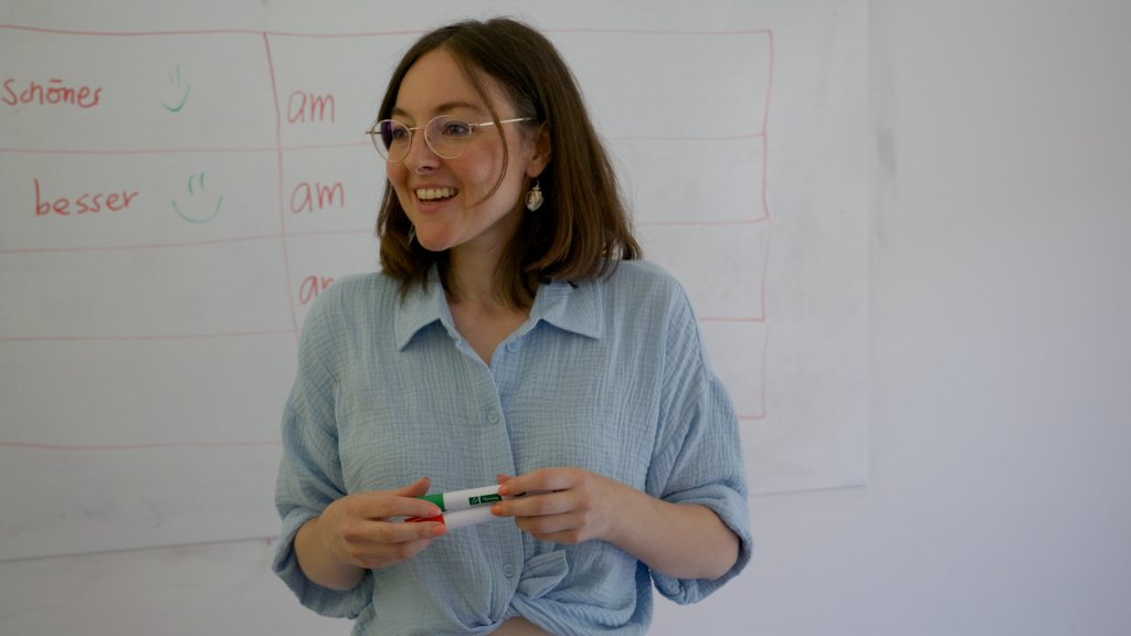 Lia Lendenmann steht vor Whiteboard, hält Marker und erklärt in einem Unterrichtsraum.