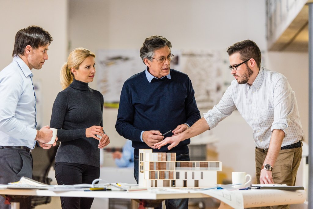 Eine Gruppe von Fachleuten, die ein Gebäudemodell in einem modernen Arbeitsplatz diskutiert.